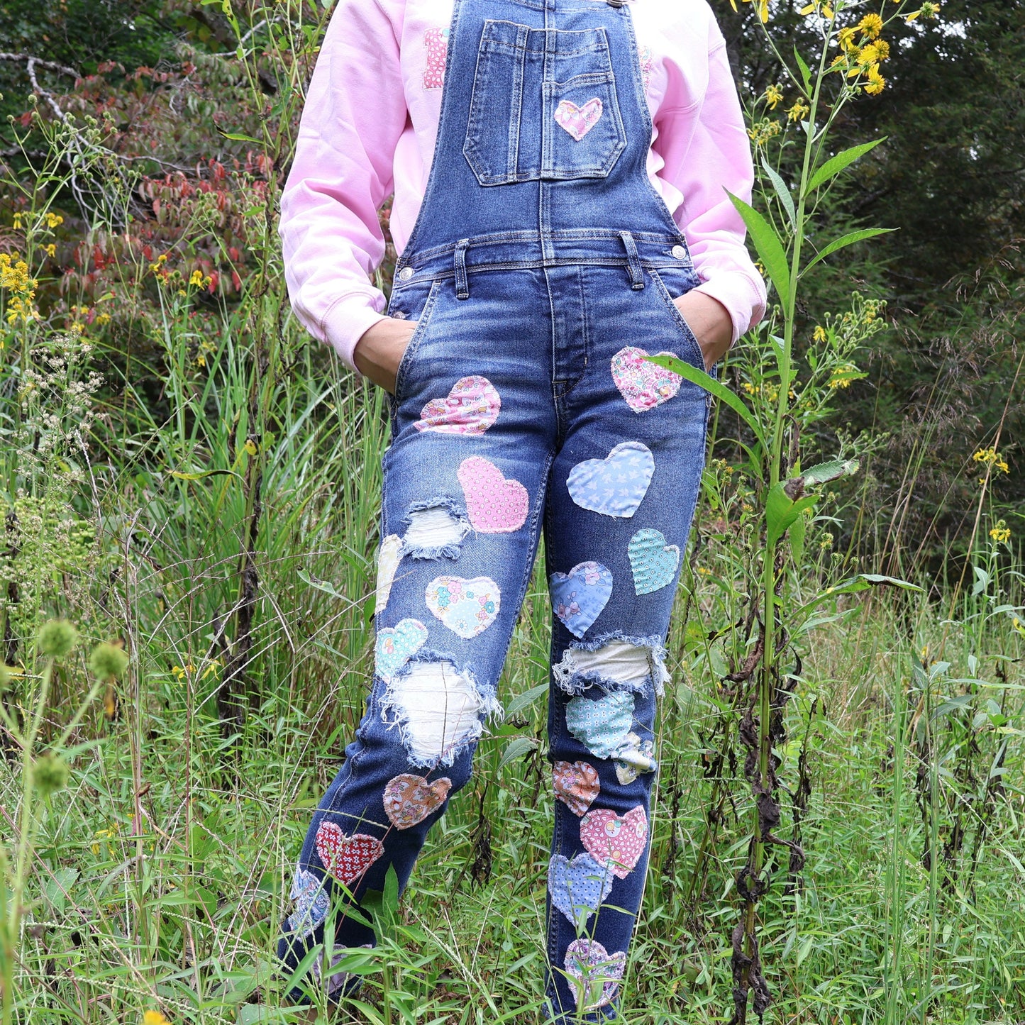 Person wearing denim overalls with colorful heart patterns in a natural setting.