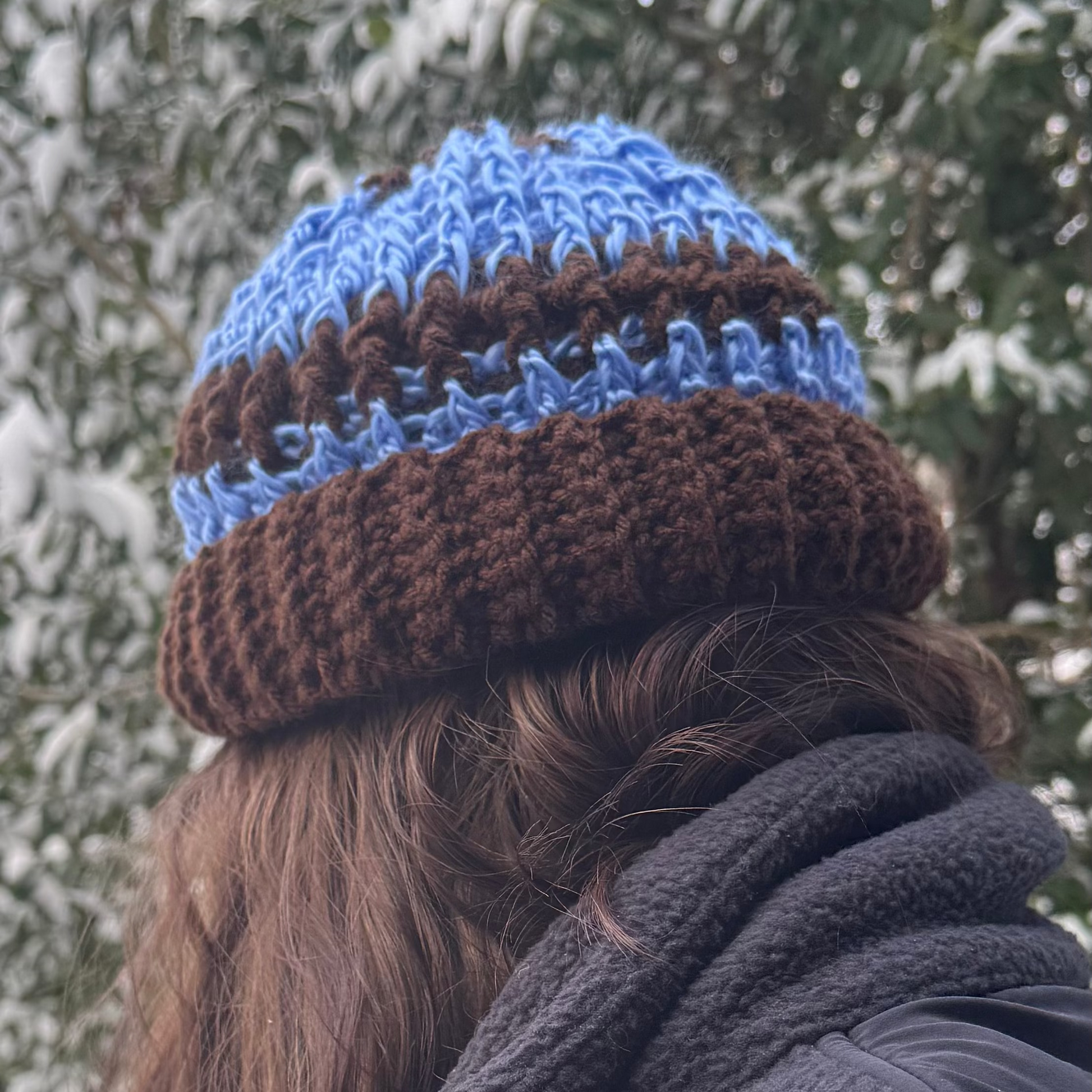 Person wearing a blue and brown knit beanie in a snowy forest setting